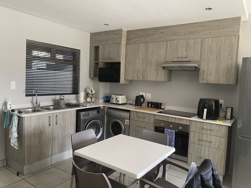 Modern kitchen featuring wood-look cabinetry, integrated appliances including an oven and cooktop, double sink, and tiled flooring with recessed lighting.