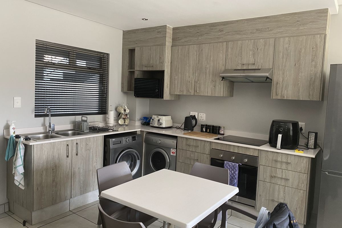 Modern kitchen featuring wood-look cabinetry, integrated appliances including an oven and cooktop, double sink, and tiled flooring with recessed lighting.