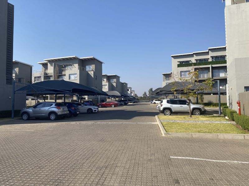 Exterior view of a modern apartment complex featuring paved parking areas with shade cloth carports and well-maintained building facades.