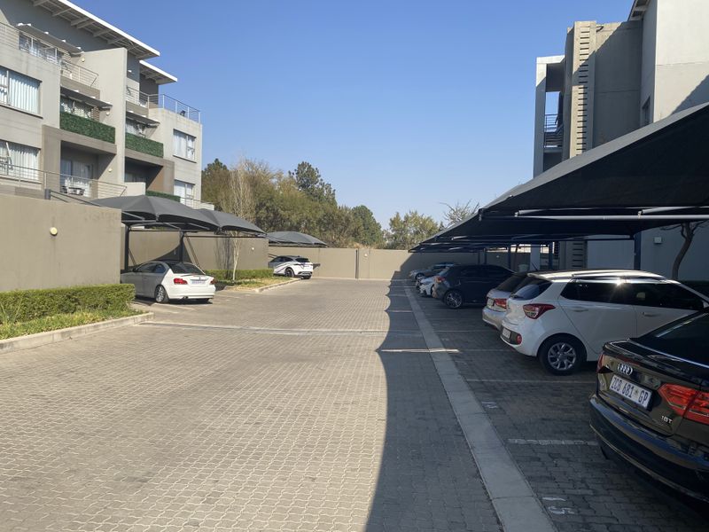 A paved parking area for the apartment complex featuring covered shade cloth parking bays and secure boundary walls.