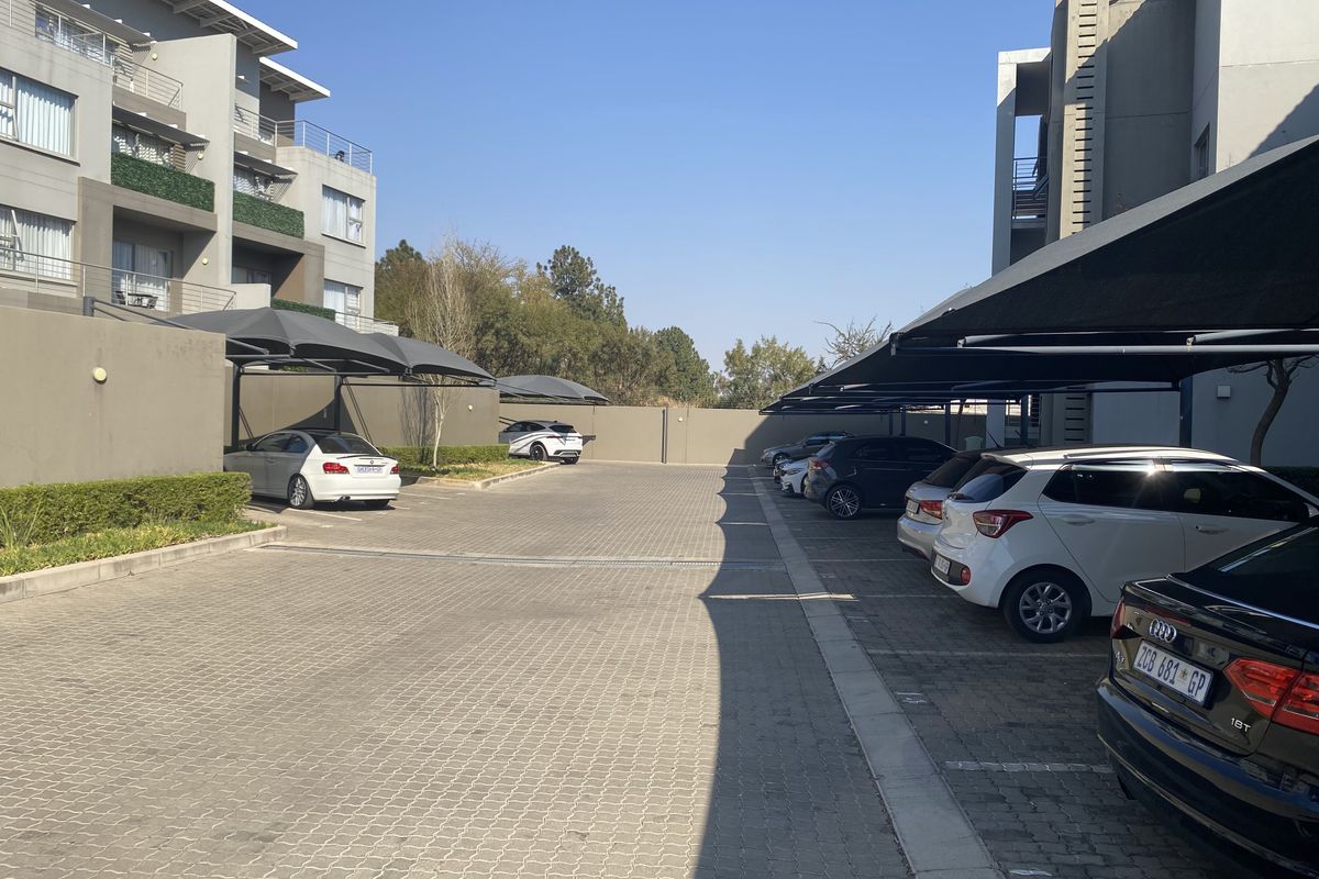 A paved parking area for the apartment complex featuring covered shade cloth parking bays and secure boundary walls.