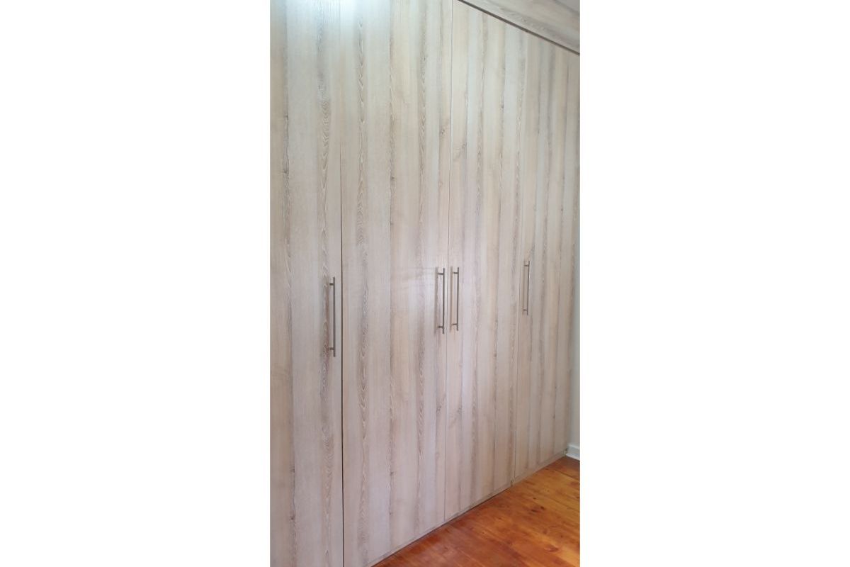 A bedroom featuring floor-to-ceiling built-in wooden wardrobes with modern metal handles and polished timber flooring.