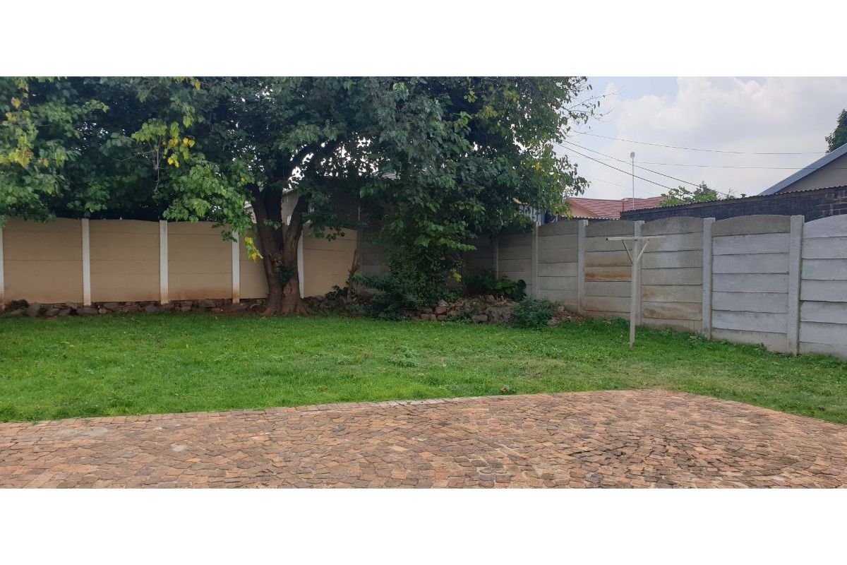 A private rear garden featuring a paved patio area, established trees, and concrete boundary walling.
