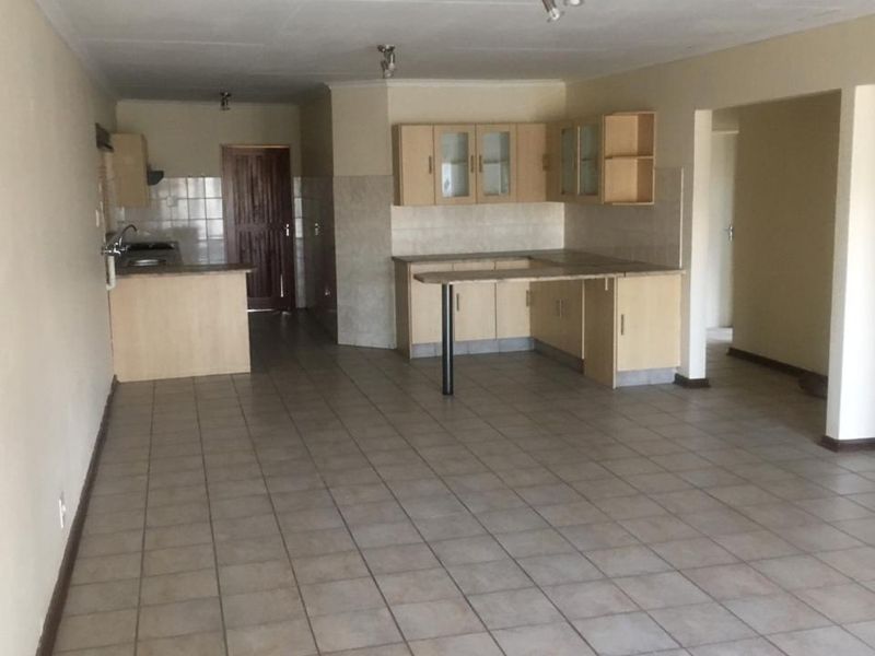Spacious open-plan kitchen and living area featuring tiled flooring, neutral walls, and functional built-in cabinetry with a breakfast bar.
