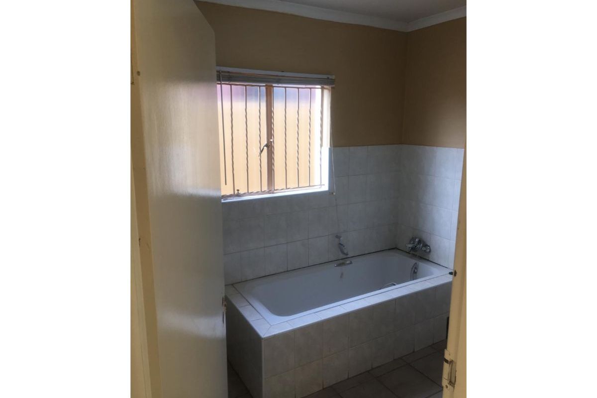 A functional bathroom featuring a built-in bathtub with tiled surround and splashback, complemented by a window with security bars.