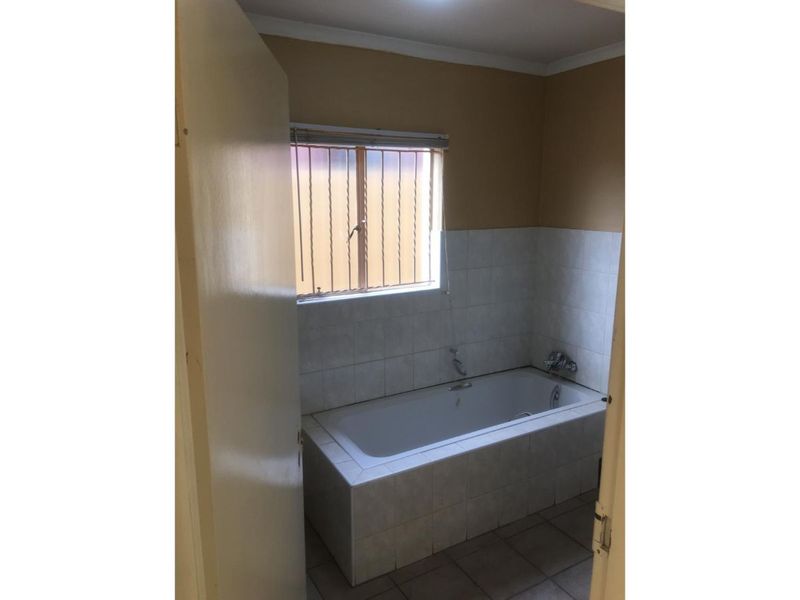 A functional bathroom featuring a built-in bathtub with tiled surround and splashback, complemented by a window with security bars.