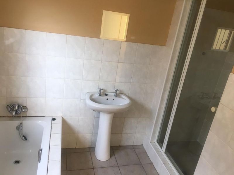 A functional bathroom featuring a pedestal basin, a built-in bathtub, and a separate shower enclosure with tiled finishes.