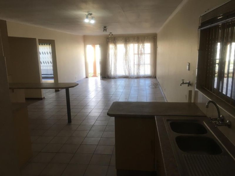 Spacious open-plan living and kitchen area featuring tiled flooring, a double bowl sink, and direct access to the exterior.