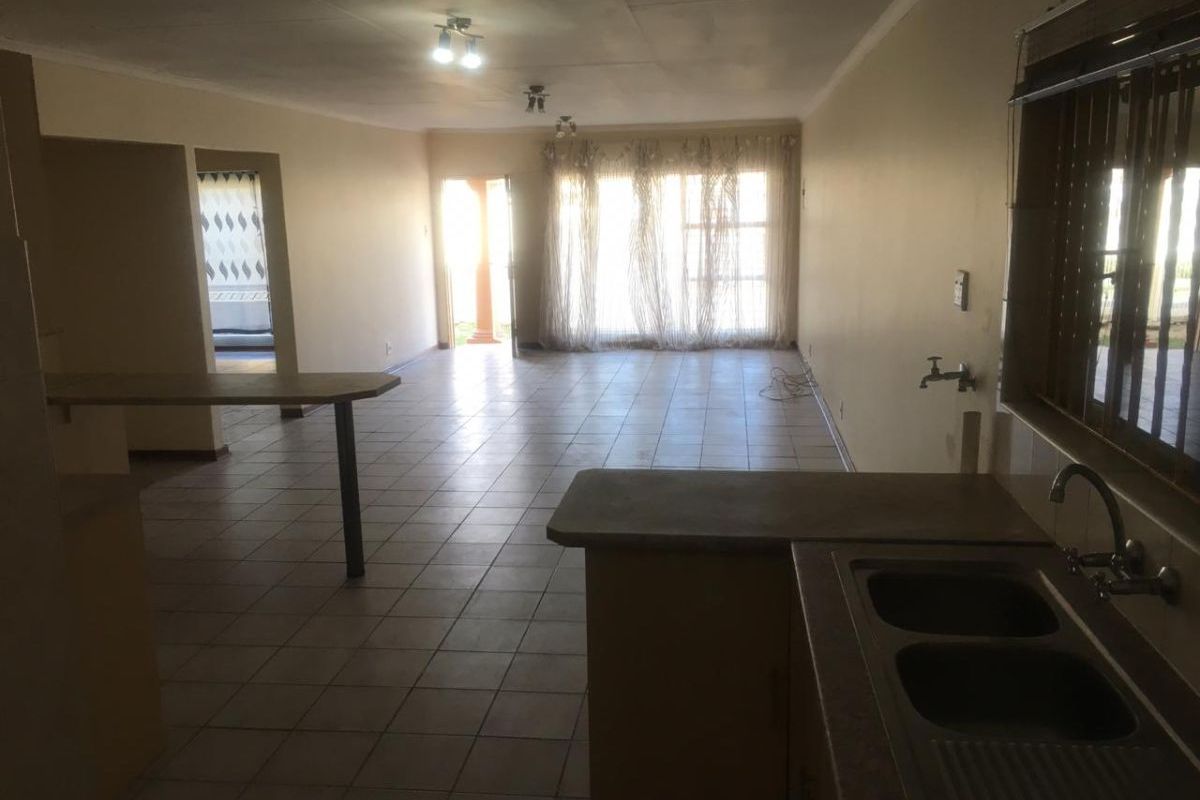 Spacious open-plan living and kitchen area featuring tiled flooring, a double bowl sink, and direct access to the exterior.