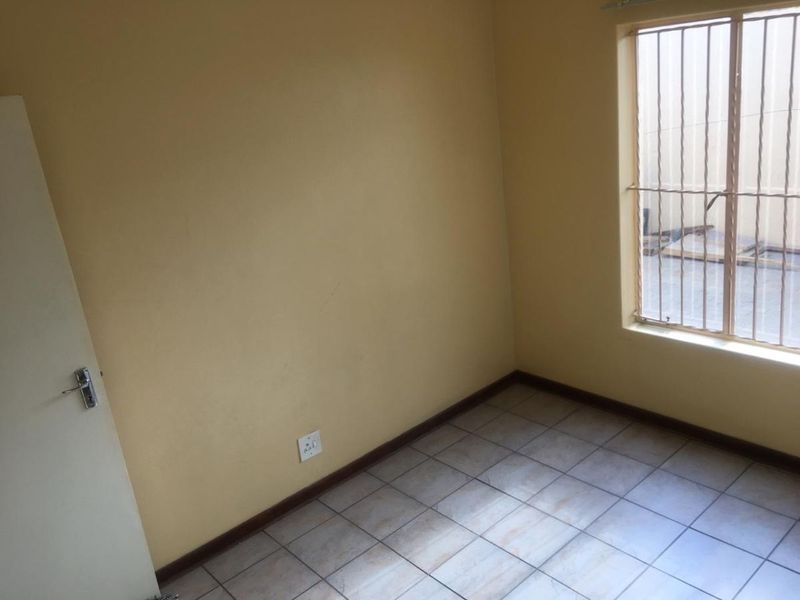 An empty bedroom featuring tiled flooring, yellow painted walls, and a window fitted with security bars.
