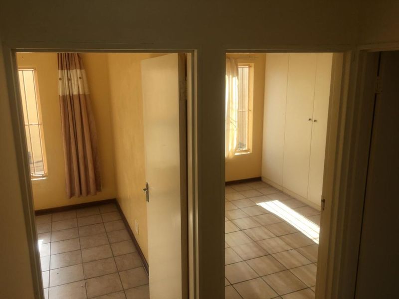 Two adjacent bedrooms featuring tiled flooring, built-in cupboards, and windows fitted with security bars.