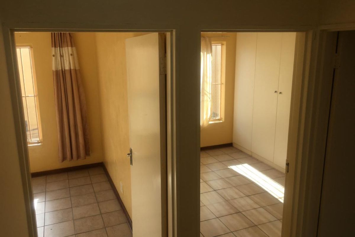 Two adjacent bedrooms featuring tiled flooring, built-in cupboards, and windows fitted with security bars.