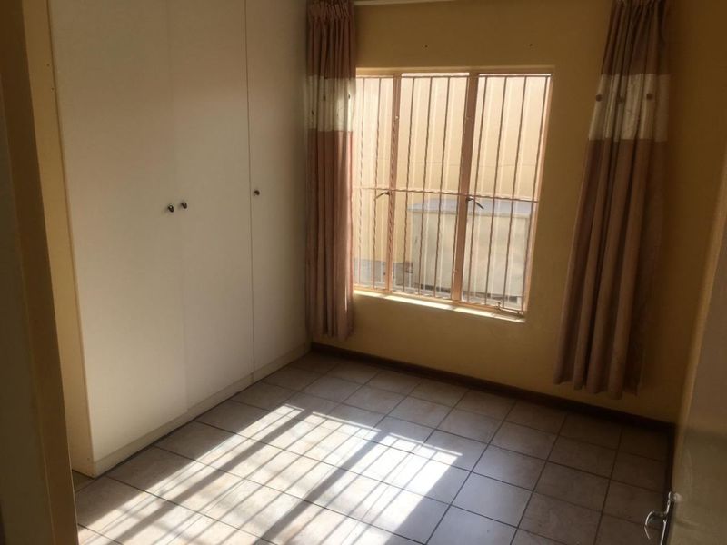 A vacant bedroom featuring tiled flooring, built-in cupboards, and security bars on the window, offering a blank canvas for potential updates.
