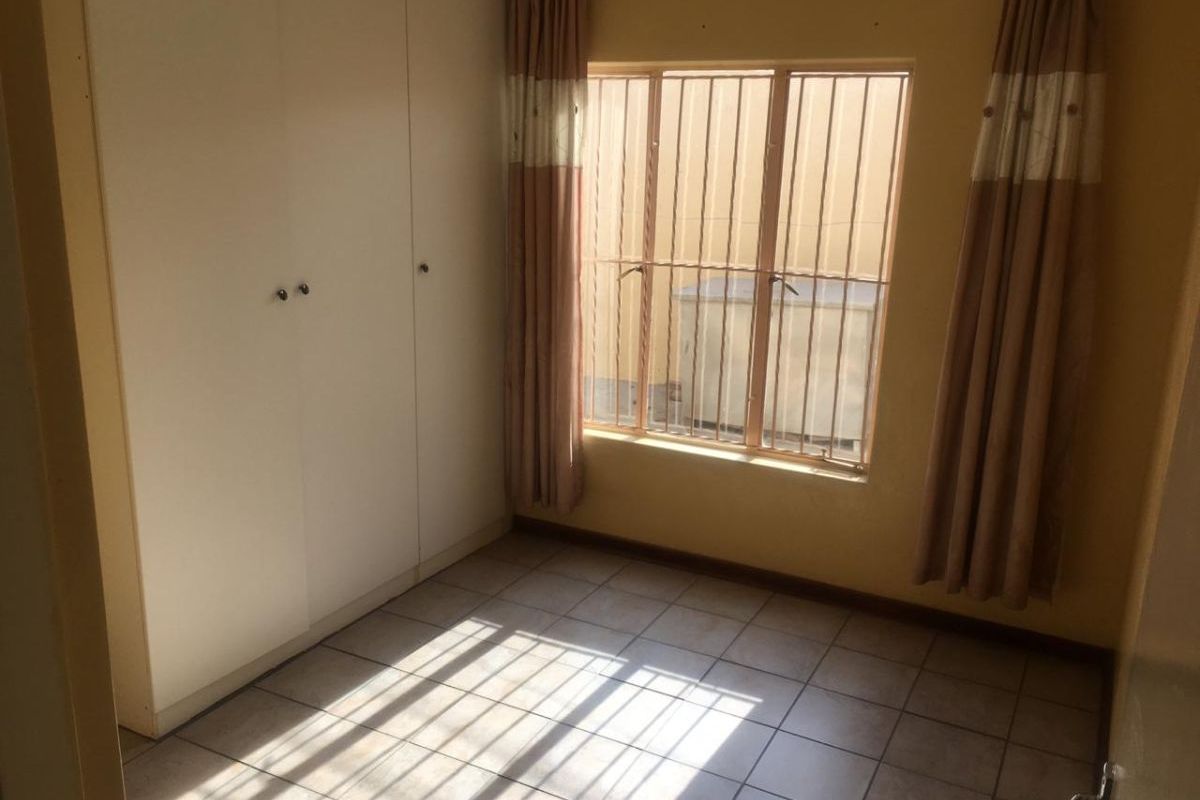 A vacant bedroom featuring tiled flooring, built-in cupboards, and security bars on the window, offering a blank canvas for potential updates.