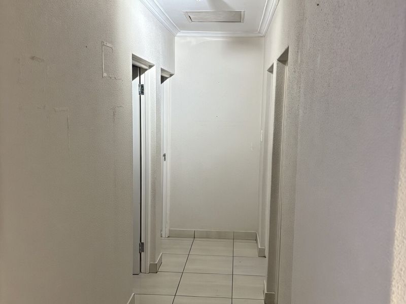 A vacant hallway featuring tiled flooring and ceiling cornice, showing signs of wear on the wall surfaces.