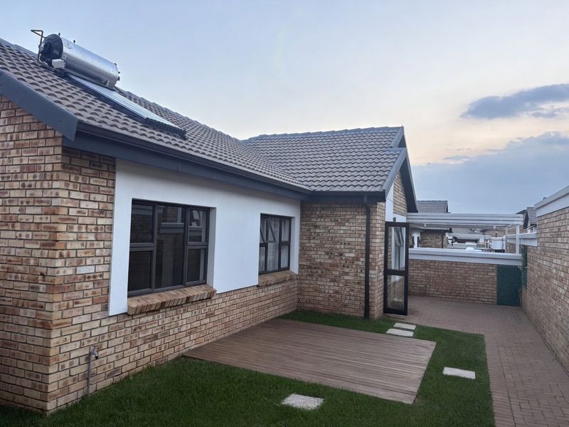 Rear exterior view of the townhouse featuring facebrick walls, a tiled roof with solar water heating, timber decking, and a paved patio area.
