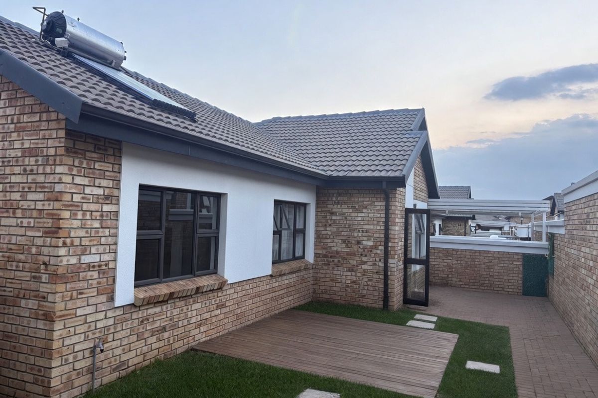 Rear exterior view of the townhouse featuring facebrick walls, a tiled roof with solar water heating, timber decking, and a paved patio area.