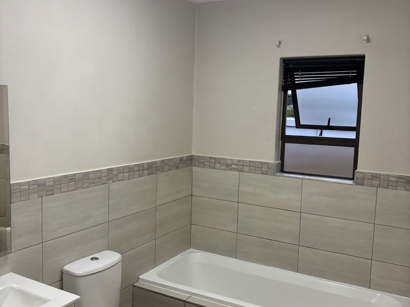 A clean and functional bathroom featuring a built-in bathtub, toilet, and vanity basin with neutral wall and floor tiling.