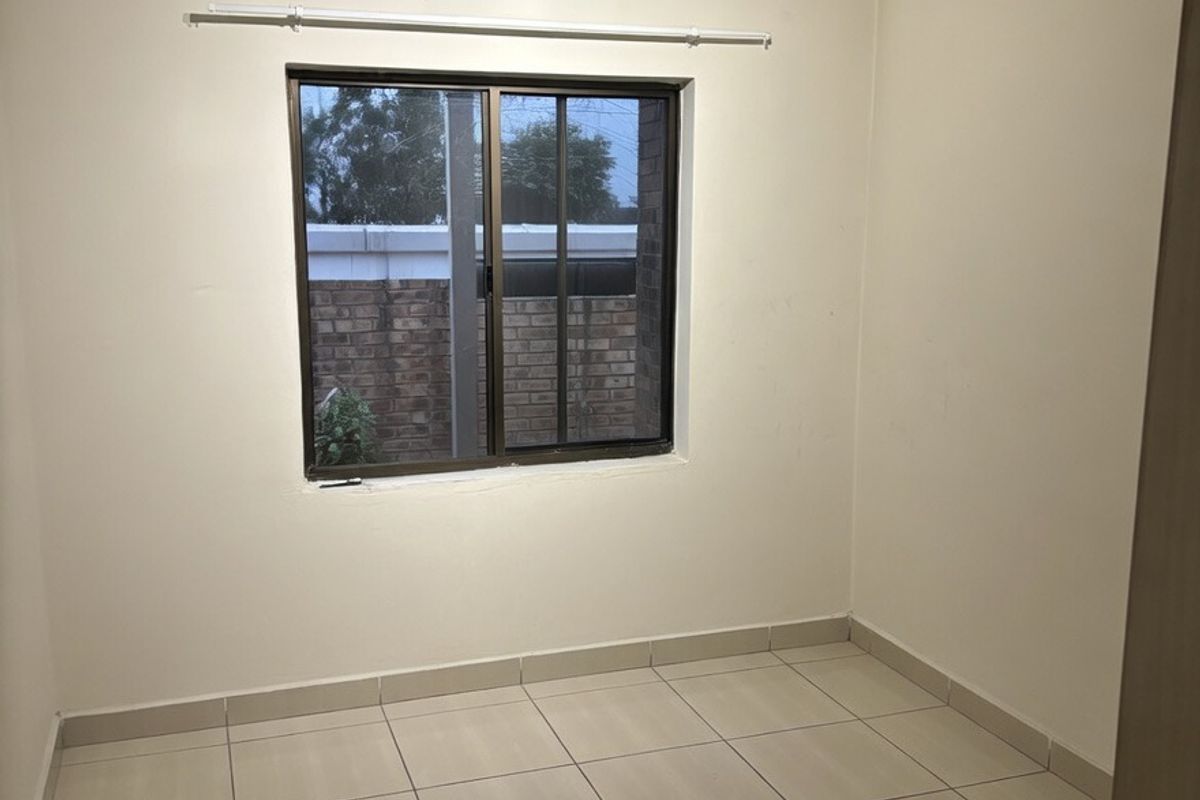 A clean, empty bedroom featuring neutral tiled flooring, a sliding window, and a modern ceiling light fixture, ready for personalization.