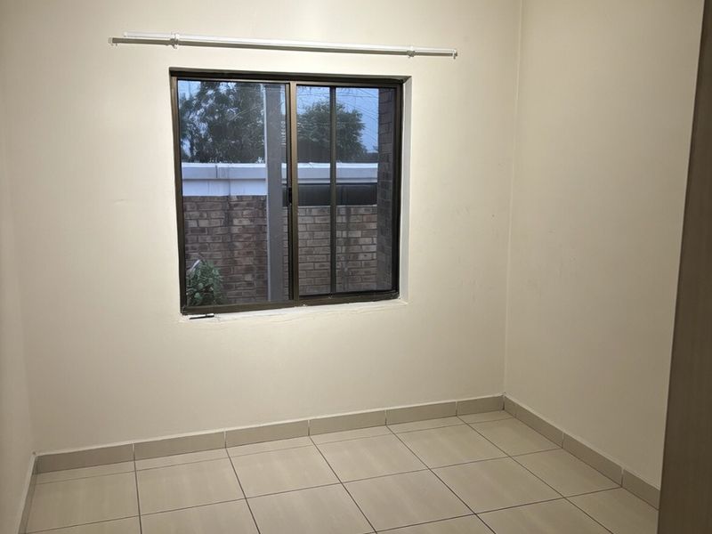 A clean, empty bedroom featuring neutral tiled flooring, a sliding window, and a modern ceiling light fixture, ready for personalization.