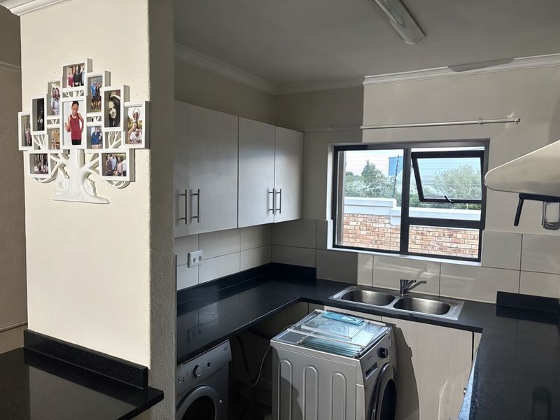 A functional kitchen featuring dark granite countertops, white cabinetry, a double stainless steel sink, and tiled splashbacks with natural light from the window.
