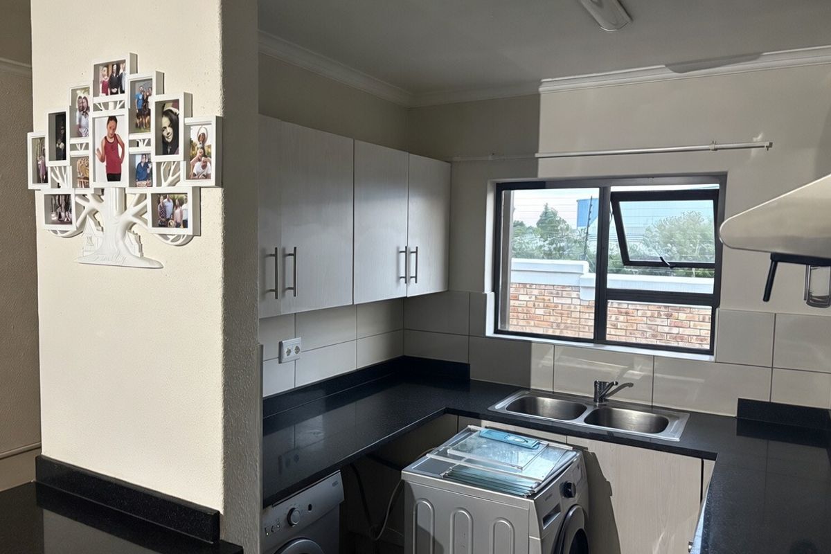 A functional kitchen featuring dark granite countertops, white cabinetry, a double stainless steel sink, and tiled splashbacks with natural light from the window.