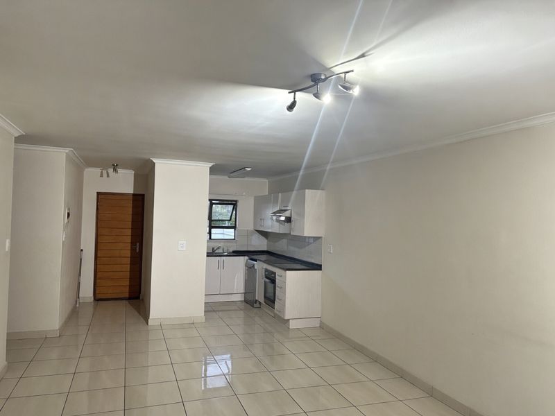 An open-plan living and kitchen area featuring tiled flooring, neutral walls, and a functional kitchen with built-in cabinetry and appliances.