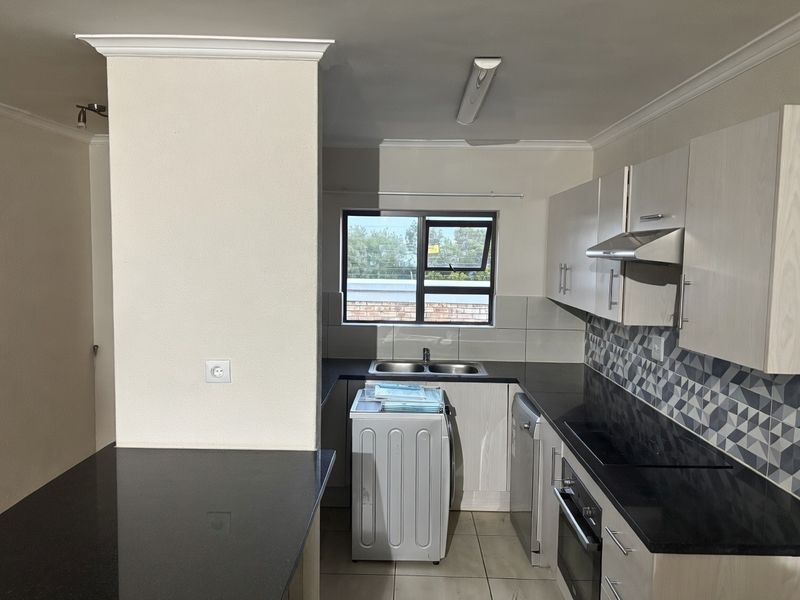 Modern kitchen featuring granite countertops, built-in oven, hob, extractor fan, and ample cabinetry with a stylish geometric tiled backsplash.