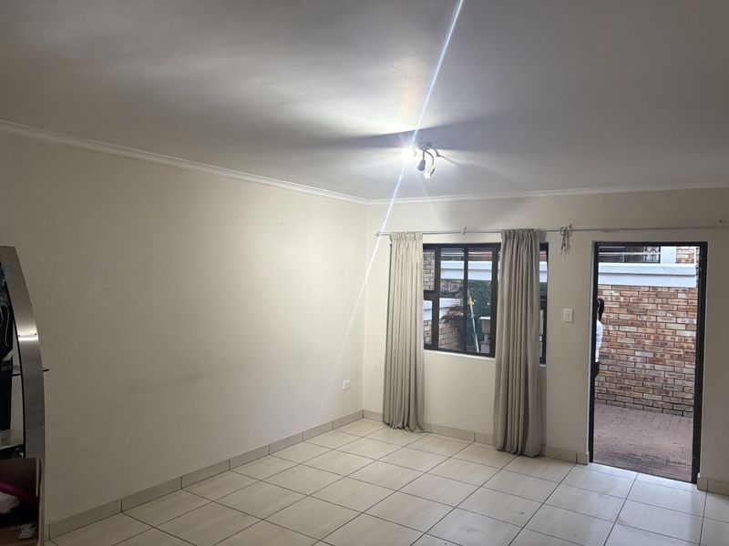 An empty living room featuring tiled flooring, ceiling coving, and direct access to an outdoor patio area through a glass-paneled door.