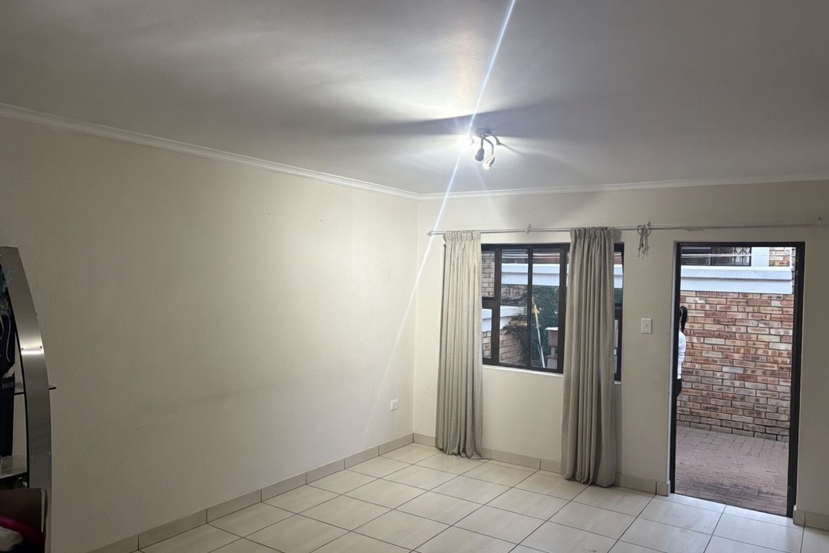 An empty living room featuring tiled flooring, ceiling coving, and direct access to an outdoor patio area through a glass-paneled door.