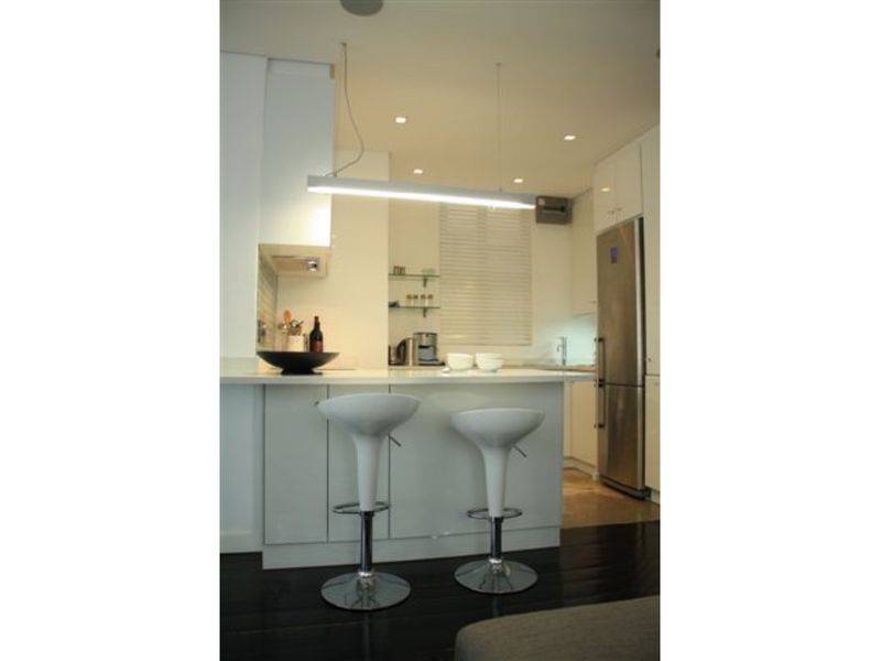Modern kitchen featuring a central island with stone countertops, sleek white cabinetry, integrated appliances, and contemporary pendant lighting.