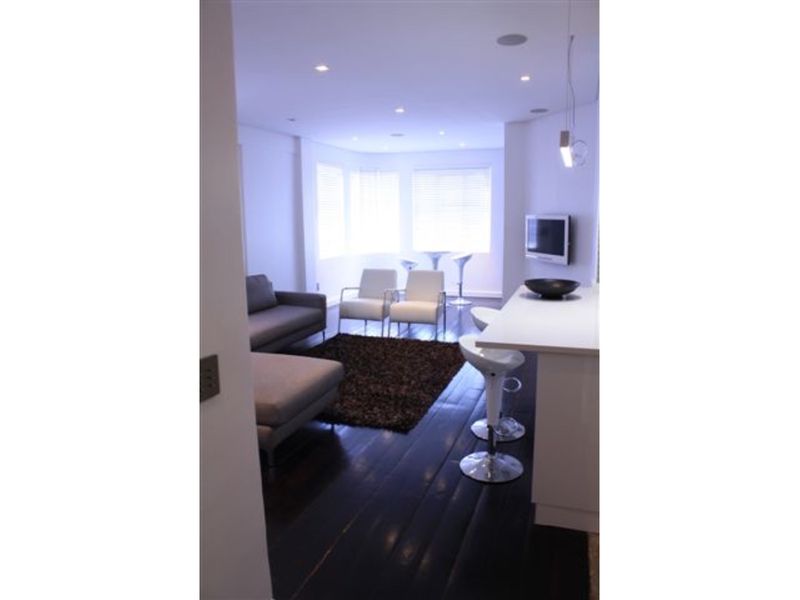 An open-plan living and kitchen area featuring dark timber flooring, recessed lighting, and a modern kitchen island with breakfast bar seating.