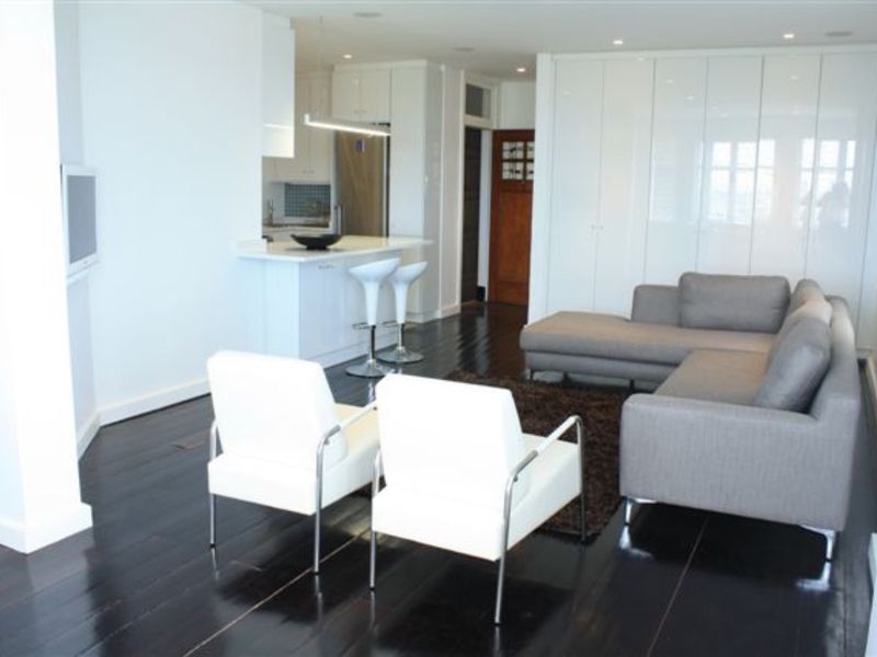 Modern open-plan living area featuring dark hardwood floors, sleek white built-in cabinetry, and a functional kitchen island with integrated appliances.