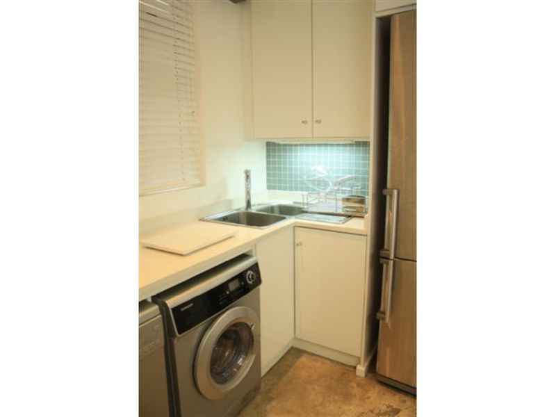 Compact laundry area featuring built-in cabinetry, a stainless steel sink, tiled splashback, and space for a washing machine.