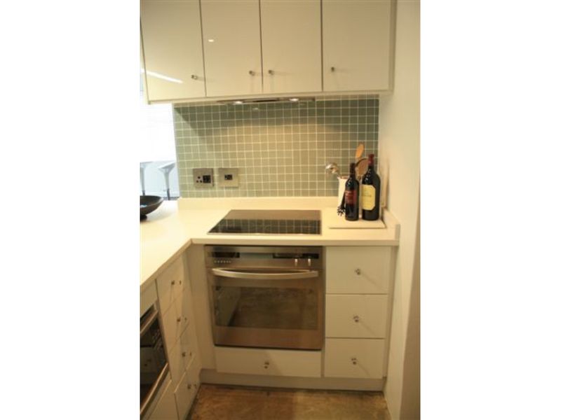 Compact kitchen featuring white cabinetry, stone countertops, a tiled backsplash, and integrated stainless steel oven and hob.