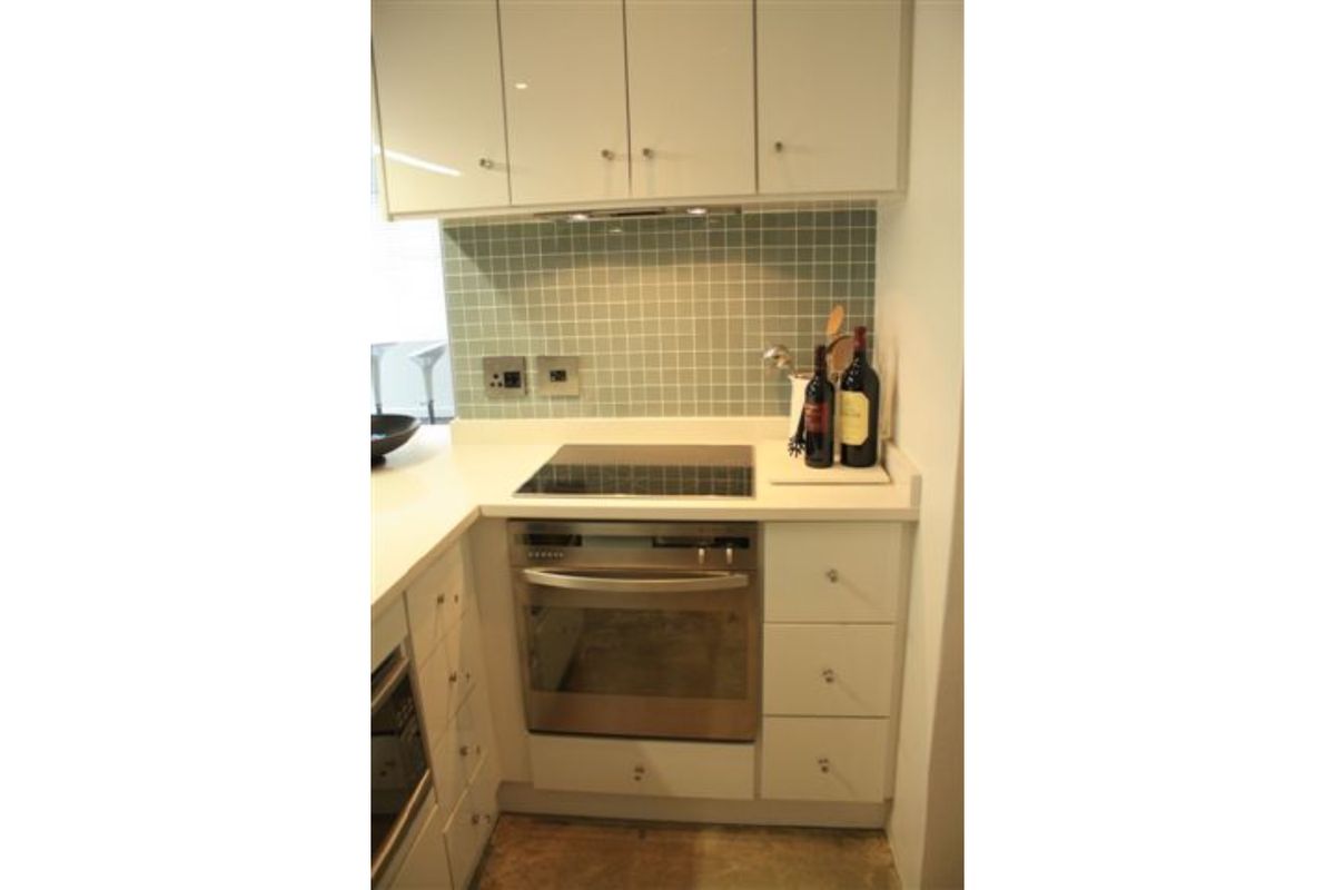 Compact kitchen featuring white cabinetry, stone countertops, a tiled backsplash, and integrated stainless steel oven and hob.