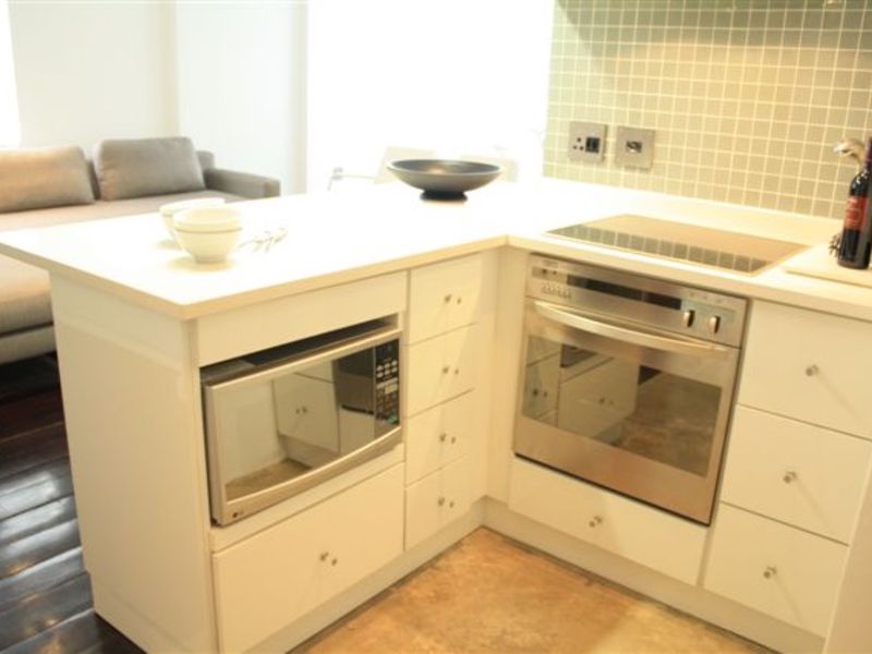 Compact kitchen area featuring white cabinetry, stone countertops, a built-in oven, electric cooktop, and a tiled backsplash.