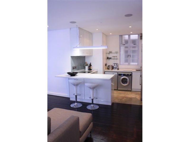 Modern open-plan kitchen featuring sleek white cabinetry, a breakfast bar, integrated laundry appliances, and dark hardwood flooring.