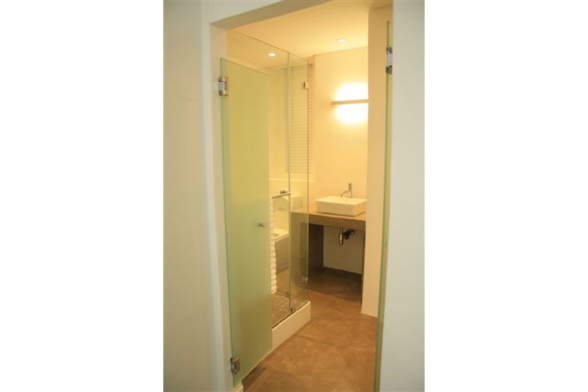 A modern bathroom featuring a glass shower enclosure, a vessel sink set on a concrete vanity, and warm recessed lighting.