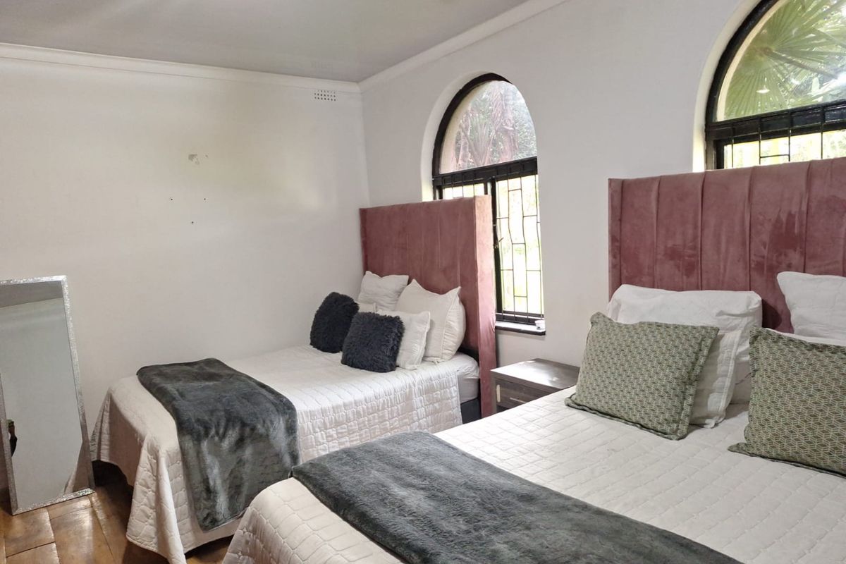 A bedroom featuring arched windows with security bars, coving, and laminate flooring, providing a functional space with potential for cosmetic updates.