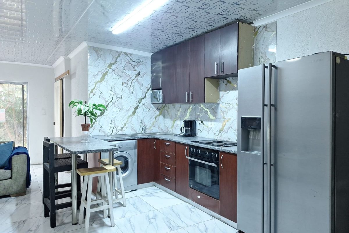 A functional kitchen featuring dark wood cabinetry, marble-effect splashbacks, a breakfast bar, and integrated appliances, with some minor cosmetic finishes requiring attention.