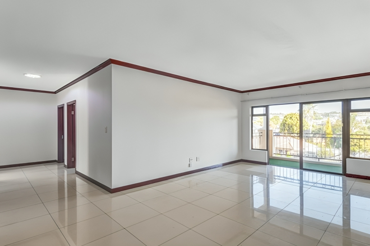 Spacious, empty living area featuring polished tile flooring, dark wood trim, and large sliding glass doors leading to a private balcony.
