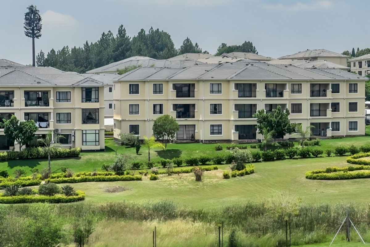 A view of the rear elevation of a multi-story apartment complex featuring balconies, tiled roofs, and well-maintained landscaped garden areas.