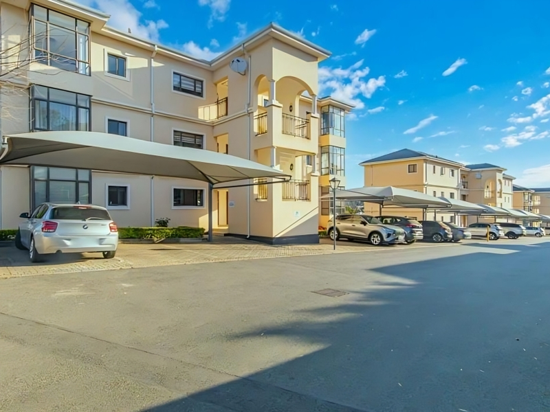 Exterior view of a multi-story apartment complex featuring paved driveway areas and dedicated shade cloth carports for residents.