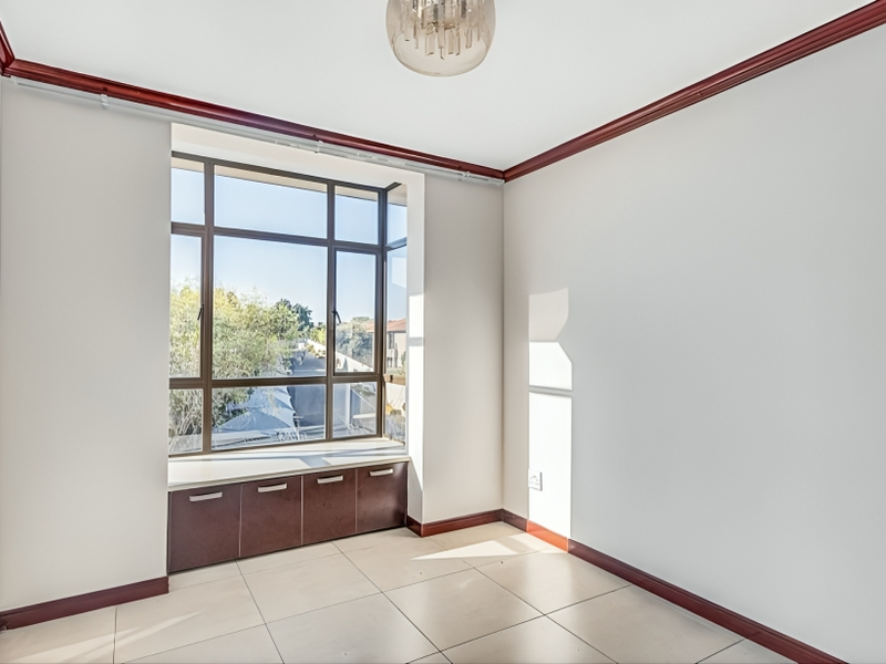 A bright, empty bedroom featuring large windows with built-in storage cabinetry, tiled flooring, and decorative crown molding.