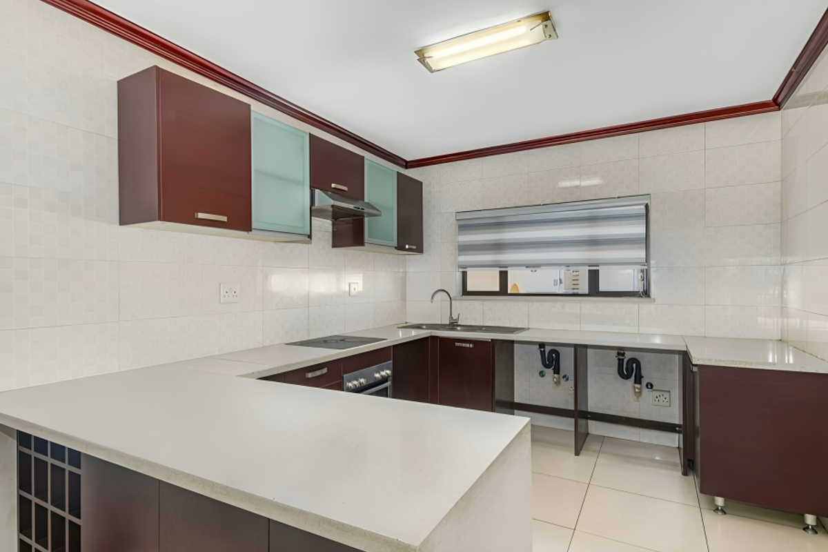 A functional kitchen featuring dark wood cabinetry, stone countertops, built-in oven and hob, and tiled finishes, with an open space ready for appliance installation.