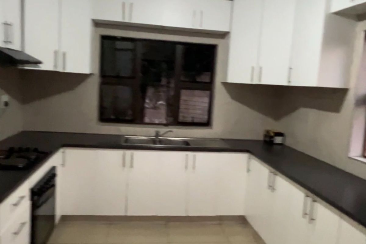 A clean, functional kitchen featuring white cabinetry, dark countertops, built-in oven, gas hob, and tiled flooring in a U-shaped layout.