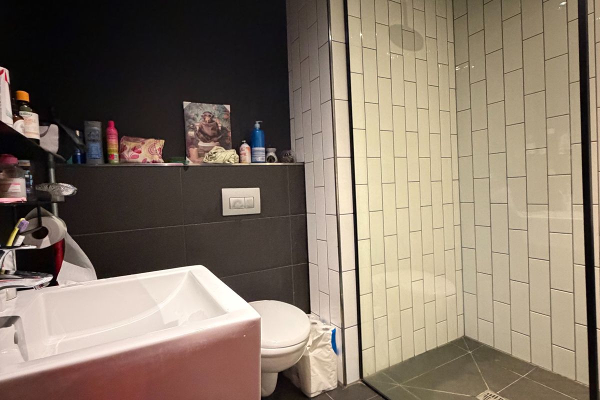 Modern bathroom featuring a walk-in shower with white subway tiles, dark floor tiling, a wall-mounted toilet, and a contemporary basin.