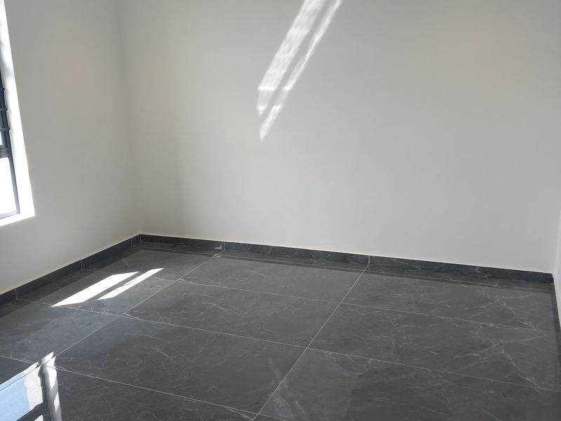 A bright, empty bedroom featuring modern large-format dark grey floor tiles and crisp white walls with recessed downlighting.