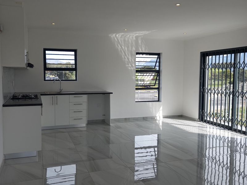 Modern open-plan living area featuring polished porcelain tiles, recessed lighting, and a compact kitchen with built-in cabinetry and gas hob.